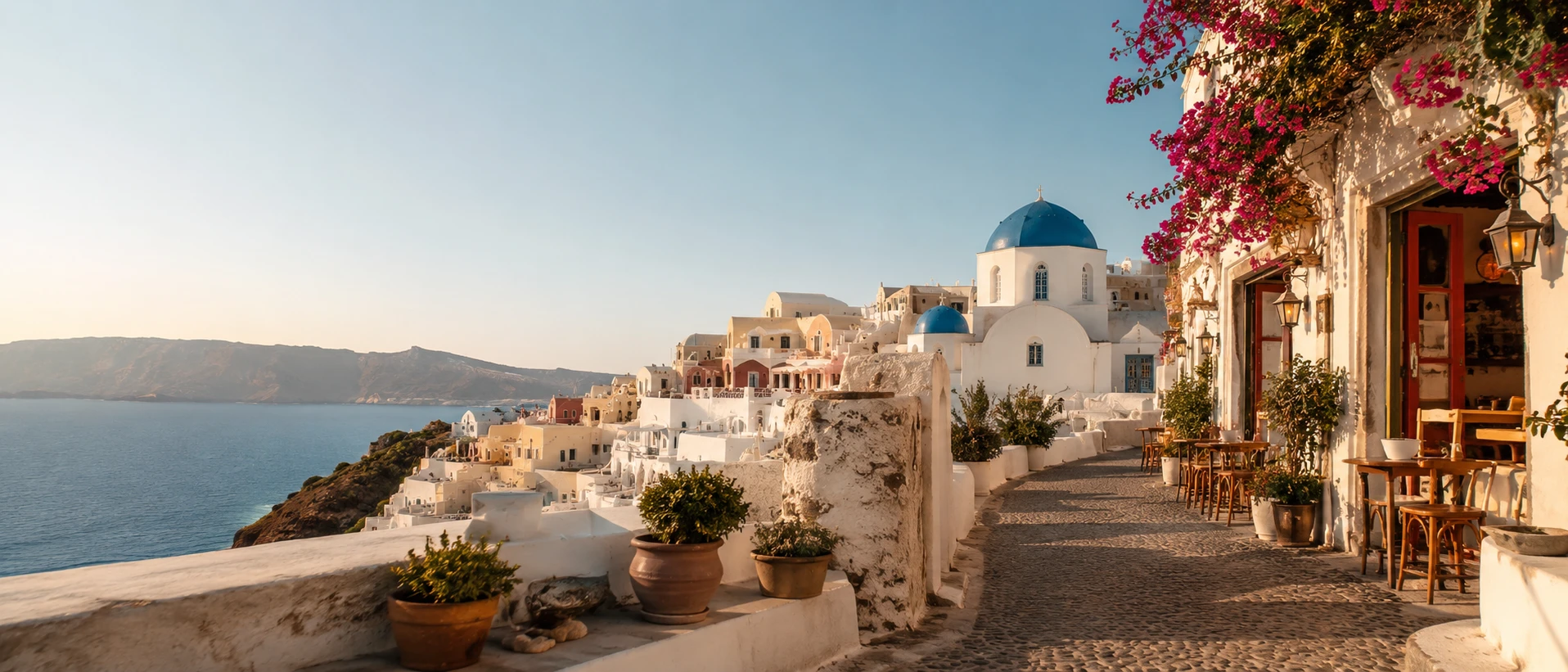 Blue-domed church and cliffside cafe overlooking the Santorini caldera at golden hour, Oia, Greece