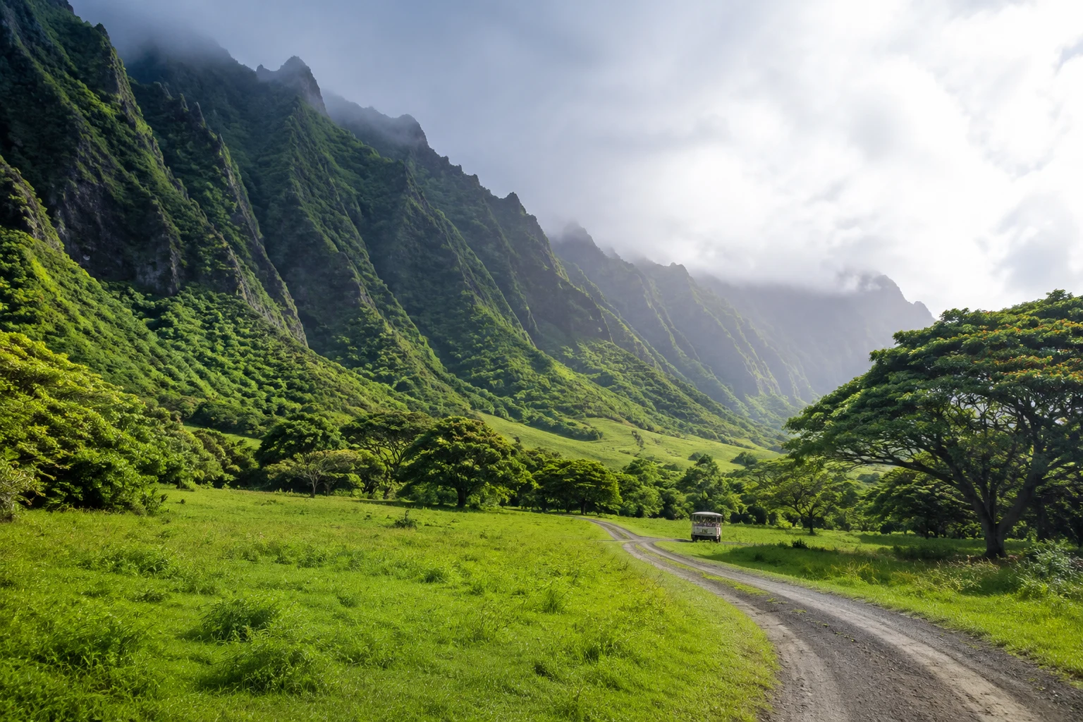 A tour vehicle on a dirt road beneath the green cliffs of Kualoa Ranch, Oahu, Hawaii