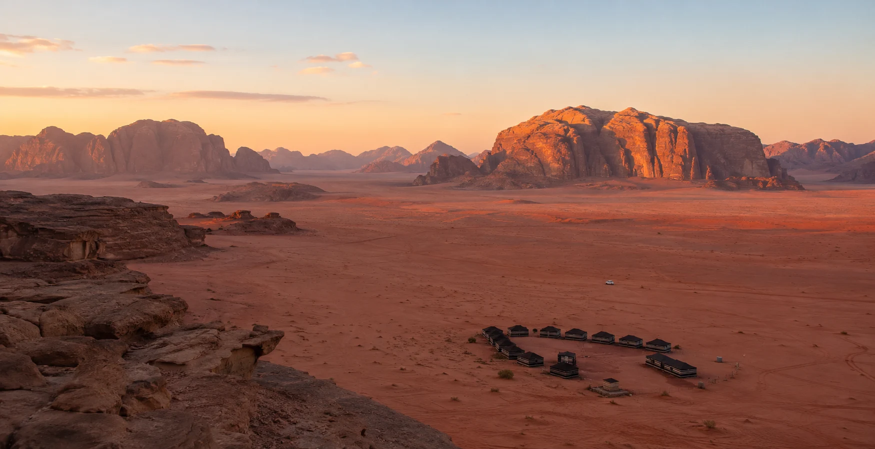 Red sandstone massifs and a desert camp at sunset in Wadi Rum, Jordan